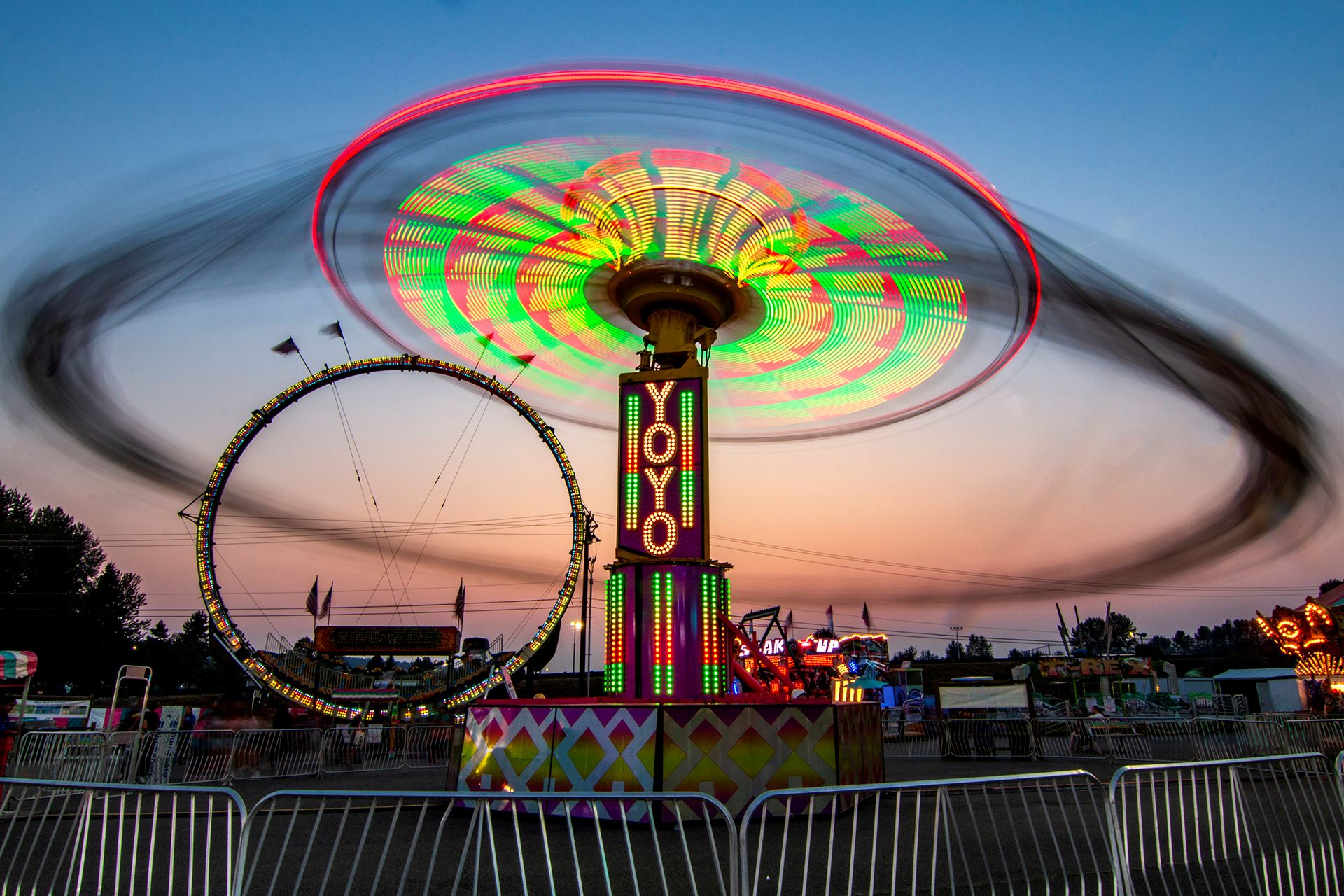 Carnival ride in at night, bright neon lights next to a setting sun